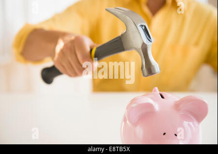 Close up of mixed race man holding hammer over piggy bank Stock Photo