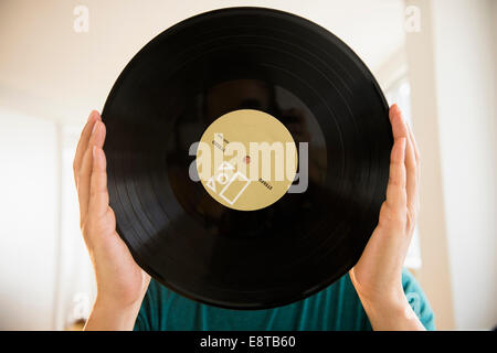 Mixed race man obscuring face with vinyl record Stock Photo