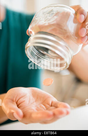 Close up of mixed race man pouring penny out of jar Stock Photo