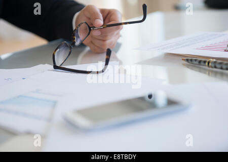 Close up of mixed race businessman holding eyeglasses at desk Stock Photo