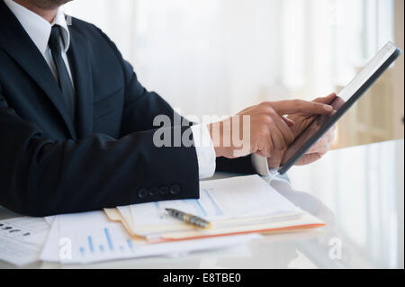 Close up of mixed race businessman using digital tablet at office desk Stock Photo