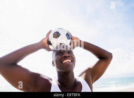 Mixed race man holding soccer ball on beach Stock Photo