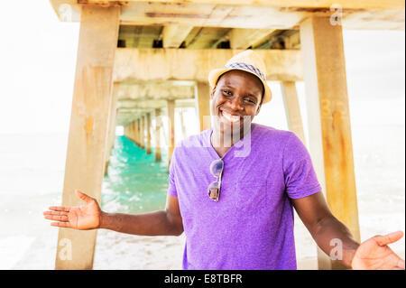 Mixed race man smiling under pier on beach Stock Photo
