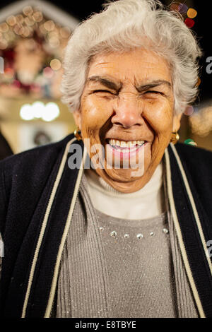 Older Hispanic woman smiling outside house decorated with string lights Stock Photo
