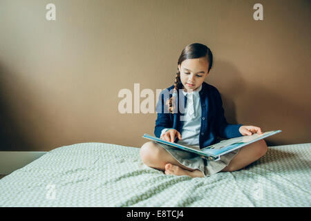 Mixed race girl reading book on bed Stock Photo
