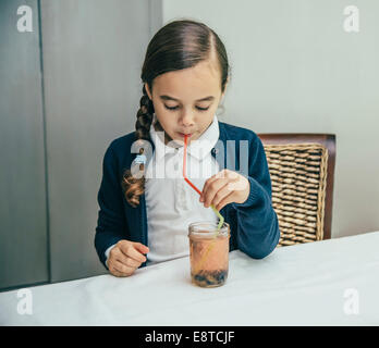 Mixed race girl drinking juice from jar through straw Stock Photo