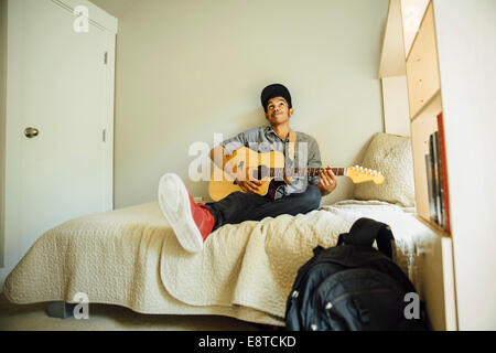Mixed race boy playing guitar in bedroom Stock Photo