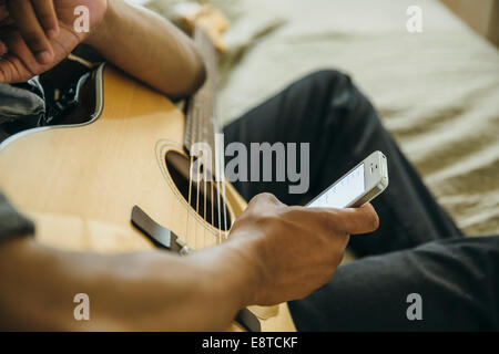 Mixed race boy with guitar using cell phone Stock Photo