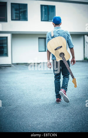 Mixed race boy carrying guitar in parking lot Stock Photo