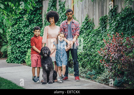 Mixed race mother and children smiling with dog on suburban sidewalk Stock Photo