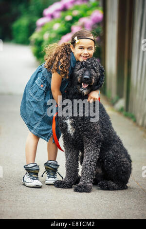 Mixed race girl hugging dog on suburban sidewalk Stock Photo