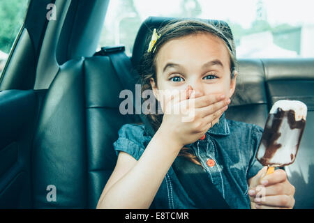 Mixed race girl eating ice cream bar in car back seat