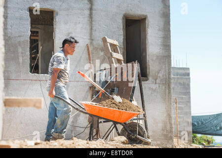 Hispanic construction worker pushing wheelbarrow at construction site Stock Photo