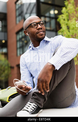 Black man listening to mp3 player in city Stock Photo