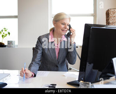 Caucasian businesswoman talking on phone at desk Stock Photo