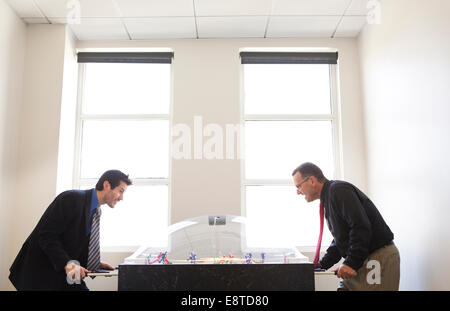 Businessmen playing foosball together in office Stock Photo