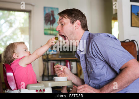 Caucasian girl feeding father from high chair