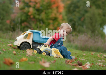 A two-year-old boy plays with toy trucks on an autumn day. Stock Photo