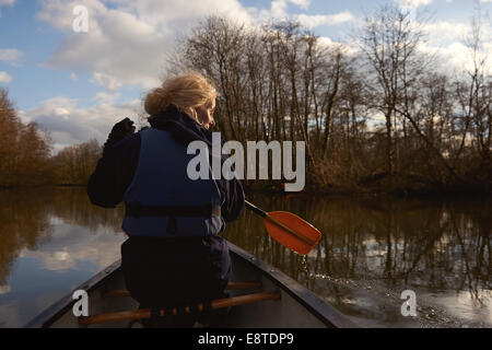 A woman in her 30's paddling in a canoe along a river on the Norfolk Broads Stock Photo