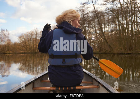 A woman in her 30's paddling in a canoe along a river on the Norfolk Broads Stock Photo