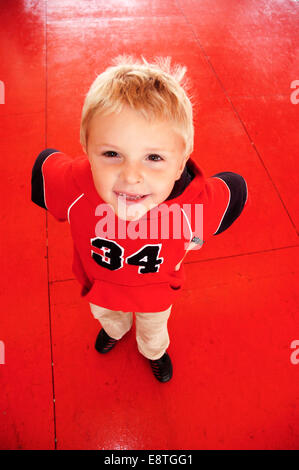 young blond boy in red top with numbers on it standing on a red floor with a happy expression Stock Photo