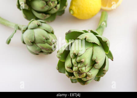 Freshly picked Globe Artichokes being prepared on a chopping board in the kitchen. Stock Photo