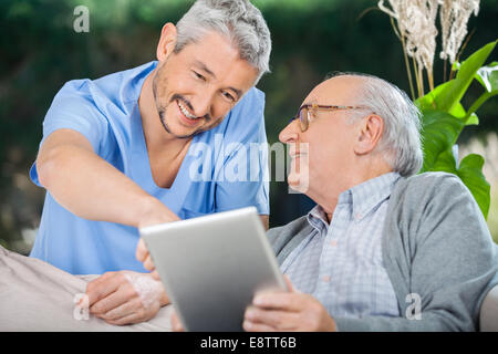Smiling Nurse Assisting Senior Man Using In Tablet PC Stock Photo
