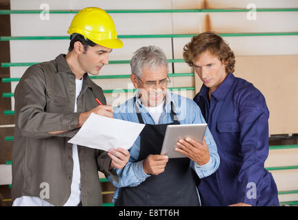 Carpenter Holding Tablet Computer While Communicating With Colle Stock Photo