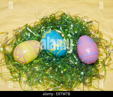 3 plastic easter eggs on green easter grass on a yellow table cloth Stock Photo
