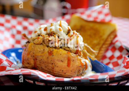 Baked potato stuffed with pulled pork BBQ and topped with sour cream and hot sauce. Stock Photo