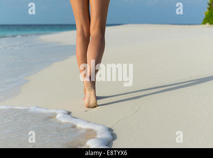 A woman walking barefoot on a beach, leaving footprints in the sand ...