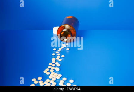 Prescription pills spilling out of bottle onto blue counter Stock Photo