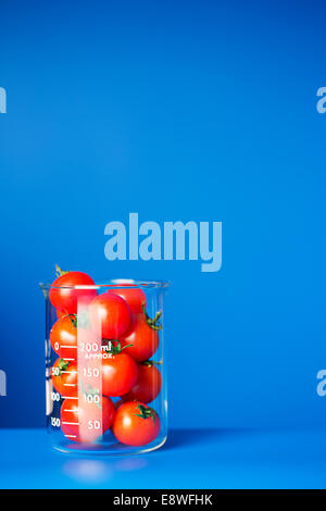 Beaker of small tomatoes on blue counter Stock Photo