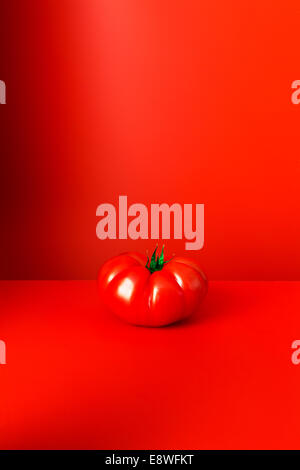 Tomato sitting on red counter Stock Photo