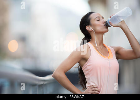 Woman drinking water after exercising on city street Stock Photo