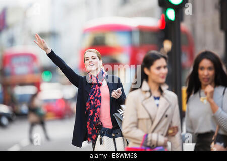 Woman signaling for taxi on city street Stock Photo