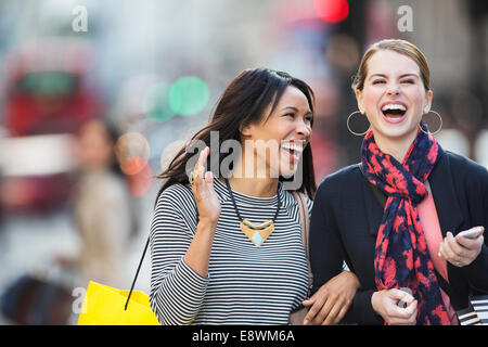 Women laughing together walking down city street Stock Photo