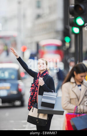 Woman hailing taxi on city street Stock Photo