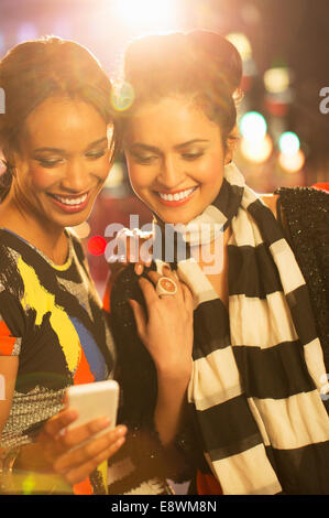 Women looking at cell phone together on city street at night Stock Photo