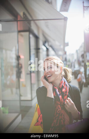 Woman talking on cell phone while walking down city street Stock Photo
