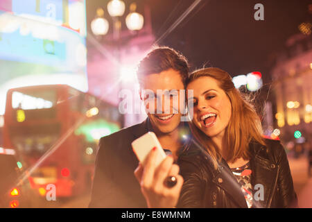 Couple taking cell phone picture together on city street at night Stock Photo