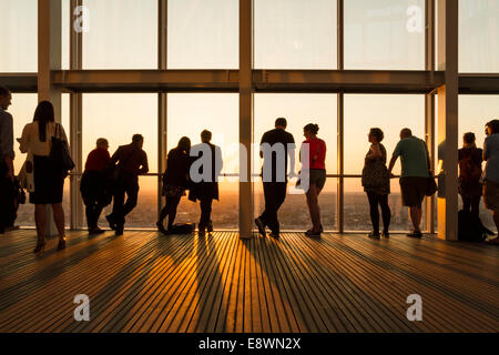 Group of people silhouetted against the the sky and setting sun while viewing London through windows at the top of The Shard, London, England, UK Stock Photo