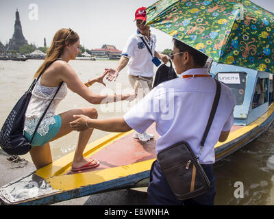 Bangkok, Thailand. 15th Oct, 2014. A tour guide (red hat) helps a woman board a tour boat on the Chao Phraya River near Wat Pho in Bangkok. The number of tourists arriving in Thailand in July fell 10.9 per cent from a year earlier, according to data from the Department of Tourism. The drop in arrivals is being blamed on continued uncertainty about Thailand's political situation. The tourist sector accounts for about 10 per cent of the Thai economy and suffered its biggest drop in visitors in June - the first full month after the army took power on May 22. Credit:  ZUMA Press, Inc./Alamy Live N Stock Photo