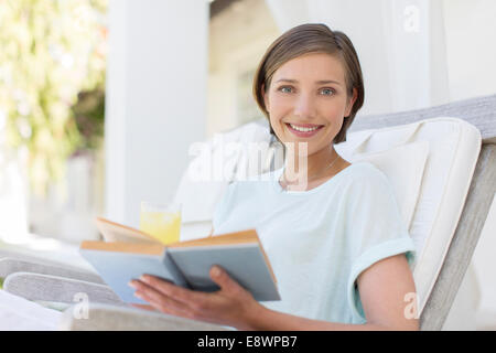 Smiling woman reading book in lawn chair Stock Photo