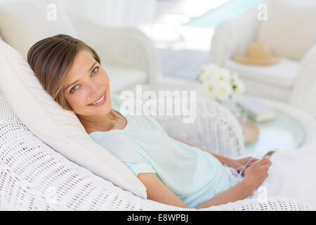 Smiling woman using cell phone in wicker chair Stock Photo