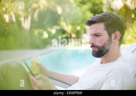 Man using digital tablet and drinking juice by swimming pool Stock Photo