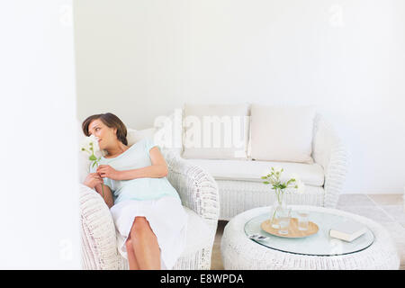 Woman smelling flowers in wicker chair in living room Stock Photo