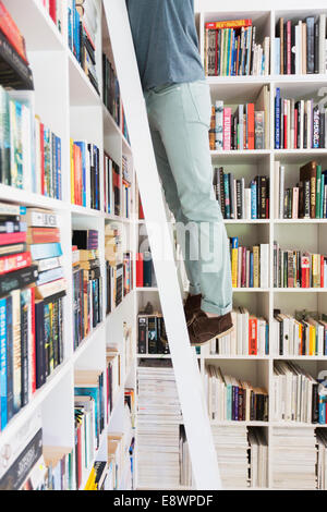 Man standing on ladder to reach books in library Stock Photo