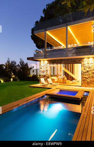 Modern house overlooking illuminated swimming pool at night Stock Photo