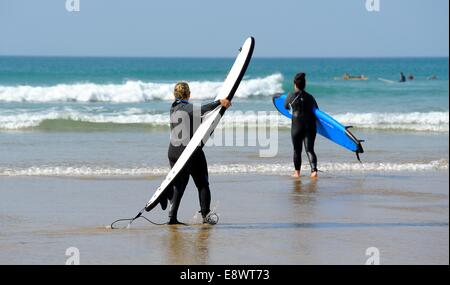 A man and a woman carrying surf boards out to sea Perranporth Cornwall England uk Stock Photo